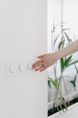 woman turn off light switch on white wall indoors