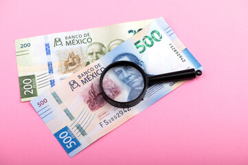 Paper currency of Mexico and magnifier on pink background, mexican pesos
