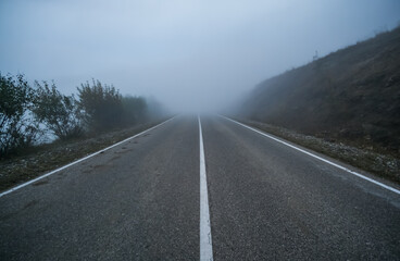 Automobile road in the mountains descending into clouds and fog in late autumn, a track with low visibility in the fog