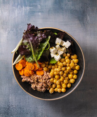 Top view of a poke bowl of chickpeas, carrot, feta cheese, tuna and lettuce.