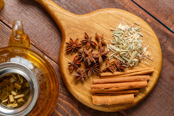 On the table on a wooden board anise, cinnamon, ginger and lemongrass grass next to a transparent...