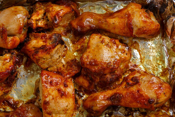 Baked chicken legs and breasts in sauce and herbs on foil close-up.