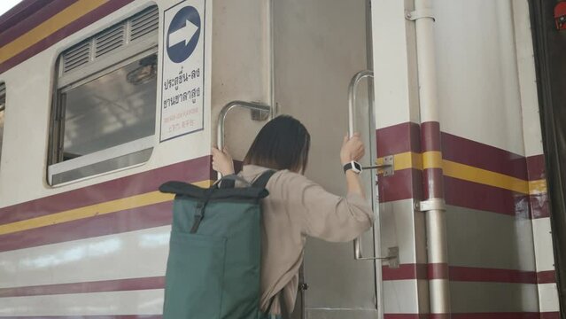 Happy Asian Woman Backpacker With Blue Backpack Grabbing The Train Railing For Safety And Stepping On The Train Going To Travel. 4k Resolution.