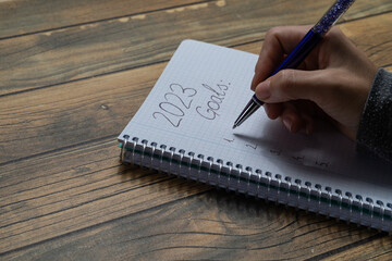 Close-up of a young woman's hand writing in a notebook her New Year's resolutions for 2023.