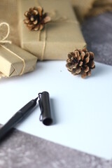 Holidays Gifts. Christmas and New Year..Gift box wrapped in brown paper, pine cones and white paper and pens placed on the table, copy space.