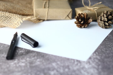 Holidays Gifts. Christmas and New Year..Gift box wrapped in brown paper, pine cones and white paper and pens placed on the table, copy space.