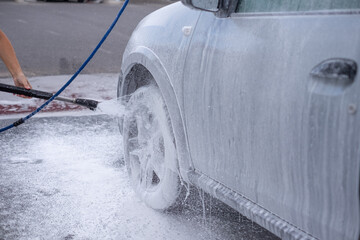 Caucasian people washing the car in a self-service car wash station using high pressure water. Car...