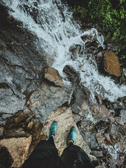 Legs from above standing on the rock near waterfall in mountains