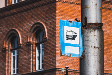 Blue and white rusty old bus stop sign on a metallic pole in an urban area with a brick building behind - 544681916