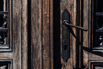 Dark wood weathered door with black handle with keyhole and iron grates