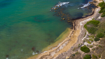 Aerial view of the Sicilian coast overlooking the Mediterranean sea, in Italy. The sea is turquoise and the beach is sandy. There is no one in the water or on the coast.