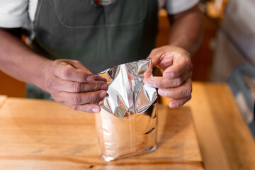 An Hispanic man is closing a bag full of ground coffee.