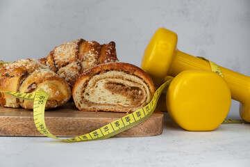 St. Martin's croissant with gym dumbbells, tape measure or measuring tape. Rogal marciński or świętomarciński. Traditional polish pastry with poppy-seed filling and nuts. Healthy diet choice concept. - obrazy, fototapety, plakaty