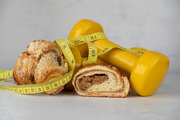 St. Martin's croissant with gym dumbbells, tape measure or measuring tape. Rogal marciński or świętomarciński. Traditional polish pastry with poppy-seed filling and nuts. Healthy diet choice concept.