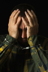 Repentant male prisoner with handcuffed hands on black background. Portrait of a man in a green...