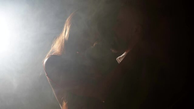 passionate embrace of beautiful woman and handsome man in darkness, medium shot in smoke