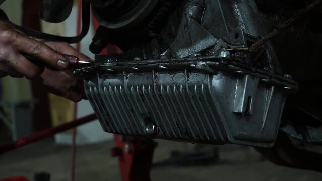 a mechanic disassembles an old dirty car engine on a red lift for repair and tuning
