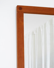 Vintage teak mid-century modern frame mirror. Warm brown wood mirror. Corner detail view with white wall and curtains. 
