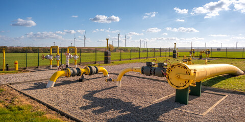 Gas pipes, natural gas transport system. Transmission infrastructure coming from the ground, yellow pipes with valve and flow meter on the background of the wind farm