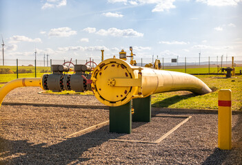 Big gas pipe - natural gas transport system. Transmission infrastructure coming from the ground, yellow pipes with a safety valve gas line on the background of the wind farm