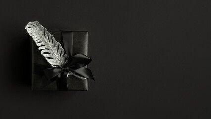 Banner with black gift box, black ribbon and silver feather on a dark background. Copyspace.