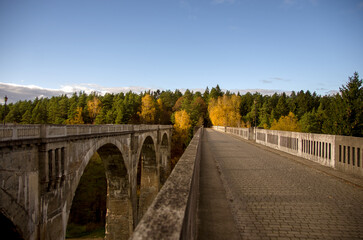 Stary betonowy most na wysokich filarach z lasem na horyzoncie na tle pięknego nieba.	
