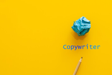 Blue text copywriter on a yellow background, next to a pencil and a crumpled piece of paper, a...