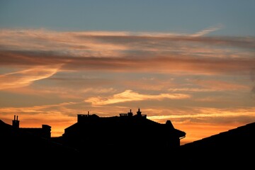 Obraz premium Amazing sunset colours looks like fire on sky over black silhouettes of roofs of city.