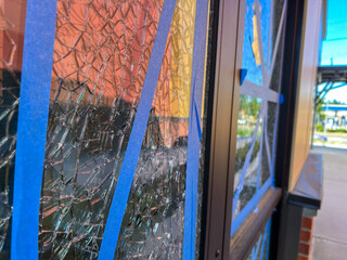 Close up, selective focus on shattered glass taped up with blue tape outside a business on a sunny...