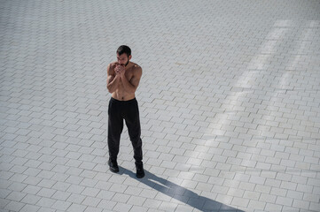 Shirtless caucasian man is getting cold and holding his hands near his face outdoors. 