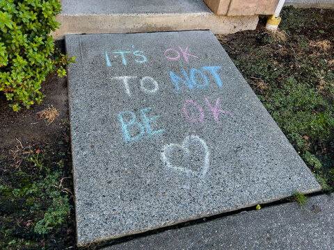 Close up view of chalk writing that says It's Okay To Not Be Okay on a sidewalk