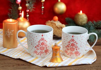 Christmas tea for two, mugs of herbal tea. Holiday decoration of golden candles, bell, coniferous...