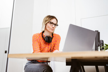 Young businesswoman with glasses works in office and looks thoughtfully at her laptop