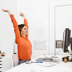 Young smiling business woman sitting in office and doing stretching exercises