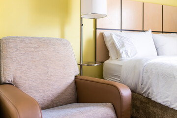 Bedroom room closeup of couch chair armseat with lamp white pillows sheets on mattress bed headboard in modern hotel motel room with nobody