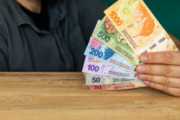 The man behind the desk is holding a bundle of Argentinian pesos, Various banknotes