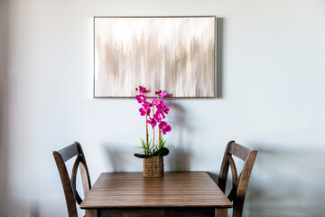 Minimalist minimalism view on two chairs by table with modern painting and orchid artificial potted flowers in pot vase by white apartment room wall