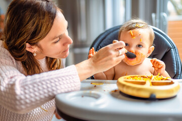 Little baby girl eating her dinner with her mother