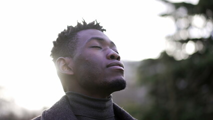 African man taking a deep breath outside at park. Close-up person meditating