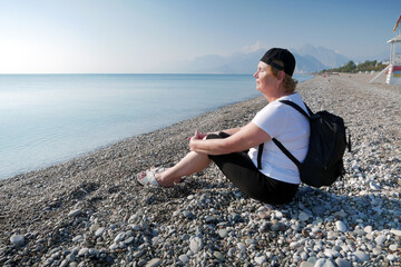 Senior adventurelsageless woman with backpack on the sea beach. Summer active tourism for pensioner.