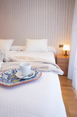 Fototapeta na wymiar Bedroom with white bed, bamboo wallpaper, gray shawl, coffee cup and tray decorated with flowers.