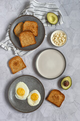 Gray kitchen table with ingredients for morning toast: avocado, fried eggs, feta cheese and toast bread. Healthy breakfast. Healthy lifestyle. Vertical photo. Top view. Flat lay food.