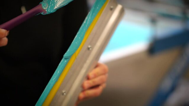 Screen printer cleaning plastisol ink off squeegee with a spatula up-close shot.