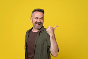 Fototapeta premium Mature handsome caucasian man beard and mustache standing isolated at yellow background Pointing to back behind with hand and thumbs up, happy and smiling confident