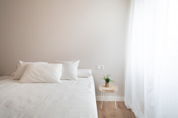Bedroom with large white bed, natural wood floor, white curtain, small table