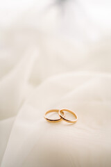 wedding rings on a white translucent chintz fabric, wedding gold rings lie on a white veil or tulle