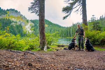 Adventurous athletic male hiking petting his Bernese Mountain Dogs on the shore of an alpine lake...