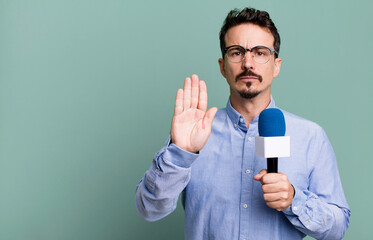adult man looking serious showing open palm making stop gesture with a microphone. presenter or...