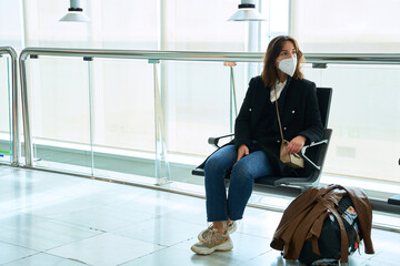 pretty brunette girl in protective mask looks away sitting at the airport with her luggage