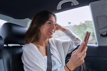 pretty girl surfs the internet with her mobile while smiling inside a car